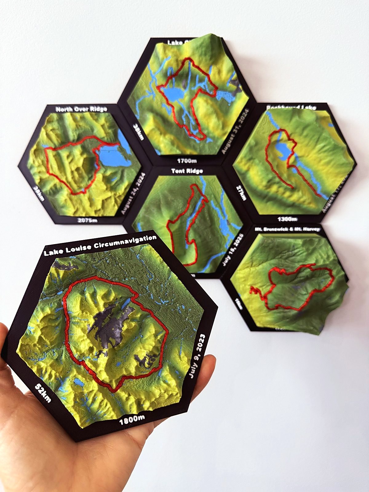 Lake Louise Circumnavigation tile held in a hand, with 52 km, 1800 m and July 9, 2023 on the frame and the route circling the mountains in red.