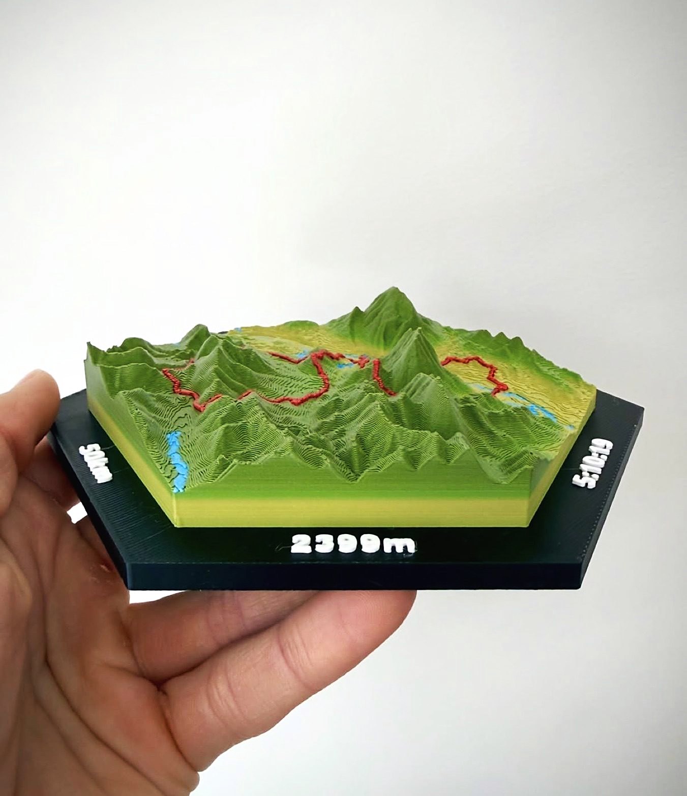 Side view of a tile held in a hand, showing mountain peaks standing up off the black hex base. The frame reads 50 km, 2399 m and 5:10:19.